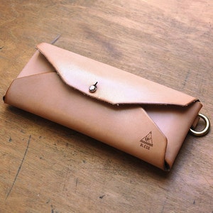 May include: A light brown leather wallet with a flap closure and a metal snap. The wallet has a triangle logo with the word "Bless" printed inside.
