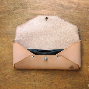May include: A light brown leather glasses case with a flap closure and a small triangle logo that says "Handmade".