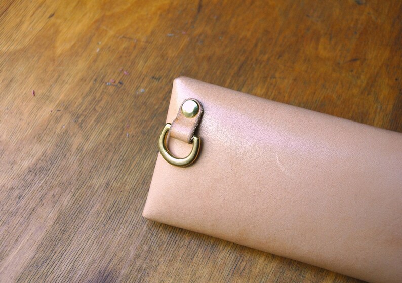 May include: A light beige leather case with a gold metal loop and a snap closure.