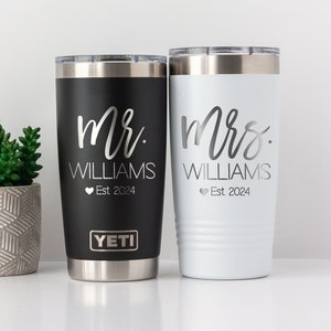 May include: Two personalized YETI tumblers, one black and one white, with the text "Mr. WILLIAMS Est. 2024" and "Mrs. WILLIAMS Est. 2024" in a silver script font.