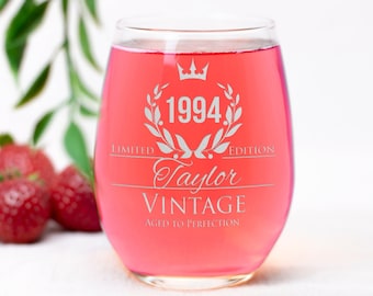 May include: A clear glass wine glass with a pink liquid inside. The glass is engraved with the text "Limited Edition 1994 Taylor Vintage Aged to Perfection".