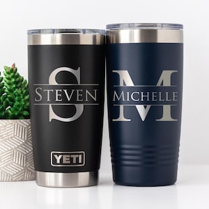 May include: Two personalized stainless steel tumblers. One is black with "Steven" and a large "S" engraved. The other is navy blue with "Michelle" and a large "M" engraved. Both have silver rims and lids.