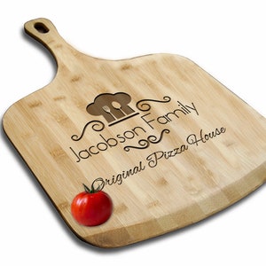 May include: A personalized bamboo pizza peel with a chef hat and utensils design. The text "Jacobson Family Original Pizza House" is engraved on the peel.