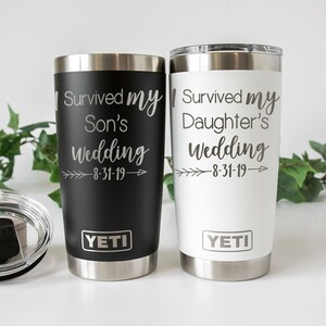 K&ouml;nnte beinhalten: Zwei YETI Becher aus Edelstahl mit schwarzen und wei&szlig;en Deckeln. Der schwarze Becher tr&auml;gt den Text "I Survived My Son's Wedding 8-31-19" und der wei&szlig;e Becher tr&auml;gt den Text "I Survived My Daughter's Wedding 8-31-19".