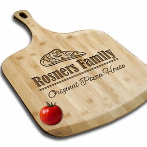 May include: A wooden pizza peel with a handle, engraved with the text "Rosners Family Original Pizza House" and a pizza slice graphic. A red tomato sits on the peel.