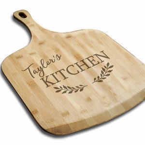 May include: A personalized bamboo cutting board with the text "Taylor's Kitchen" and a decorative leaf design.