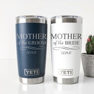 K&ouml;nnte beinhalten: Zwei YETI Becher aus Edelstahl in wei&szlig; und blau. Die Becher sind mit dem Text "Mutter des Br&auml;utigams" und "Mutter der Braut" sowie dem Datum "02.24.20" graviert.