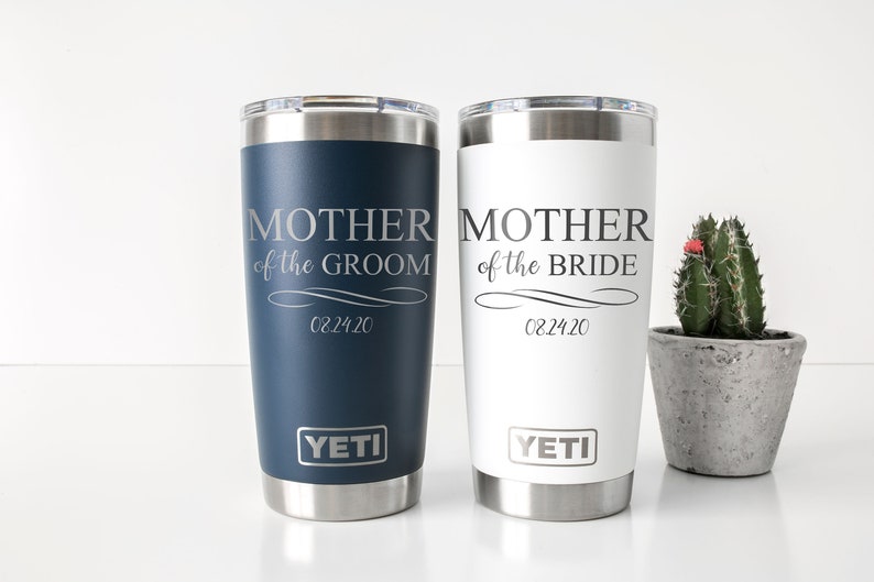 K&ouml;nnte beinhalten: Zwei YETI Becher aus Edelstahl in wei&szlig; und blau. Die Becher sind mit dem Text "Mutter des Br&auml;utigams" und "Mutter der Braut" sowie dem Datum "02.24.20" graviert.