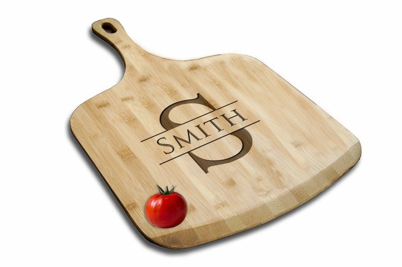 May include: A personalized bamboo cutting board with a large "S" initial and the name "SMITH" engraved on it. A red tomato is sitting on the board.