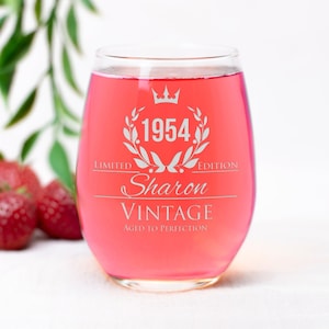 May include: A clear wine glass with a pink liquid inside. The glass has a white design that says "Limited Edition 1954 Sharon Vintage Aged to Perfection".