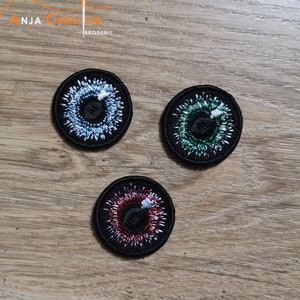 Peut inclure: Trois patchs oculaires brodés de différentes couleurs. Les patchs oculaires sont noirs avec une pupille blanche et un iris coloré. Les couleurs sont le bleu, le vert et le rouge.