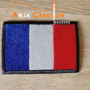 Op de afbeelding: Geborduurde patch met het ontwerp van de Franse vlag met blauwe, witte en rode verticale strepen. De patch heeft een zwarte rand en de tekst "ANJA CREATION BRODERIE" in oranje en wit.