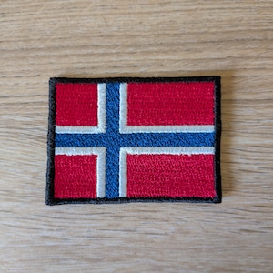 Op de afbeelding: Een rechthoekige geborduurde patch met de vlag van Noorwegen. Het ontwerp bestaat uit een rood veld met een blauw Scandinavisch kruis omlijnd in wit. De gehele patch is afgewerkt met een dikke, zwarte gestikte rand voor een strakke afwerking.