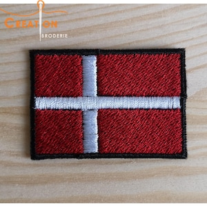Könnte beinhalten: Roter und weißer gestickter Patch der dänischen Flagge mit schwarzem Rand.