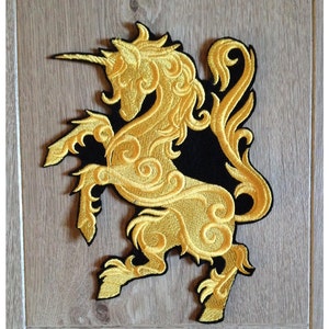 Op de afbeelding: Een gouden geborduurde patch met een gedetailleerd eenhoorn. Het eenhoorn staat op zijn achterpoten met zijn hoorn naar voren gericht. De patch is op een zwarte achtergrond.