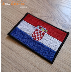 May include: An embroidered patch of the Croatian flag. The flag is red, white and blue with a coat of arms in the centre. The coat of arms features a chequered shield with a crown on top.