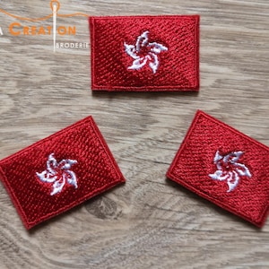 Peut inclure: Trois patchs brodés rouges avec un motif de fleur stylisé blanc. Les patchs sont sur une surface en bois.