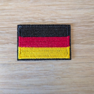 Peut inclure: Un écusson brodé rectangulaire représentant le drapeau tricolore horizontal de l'Allemagne. Le motif se compose de trois bandes horizontales égales de couleur noire en haut, rouge au milieu et jaune doré en bas, bordées d'une couture noire.