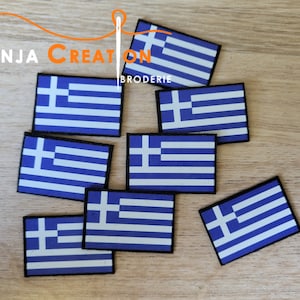 May include: Eight embroidered Greek flag patches on a wooden surface. The patches are blue and white with a white cross in the center. The patches are approximately 2 inches by 3 inches.