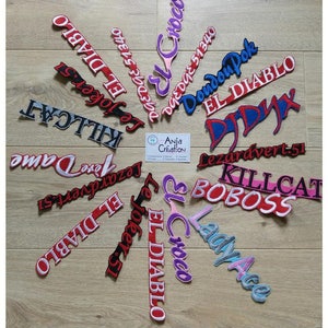 Peut inclure: Une collection de patchs brodés colorés avec différents noms et expressions, notamment "El Diablo", "Killcat", "Boboss", "Lady Ace", "Lezardvert.51" et "Doudou Dok".