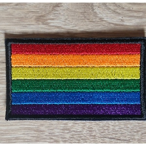 Peut inclure: Un patch de drapeau arc-en-ciel de la fierté avec six bandes horizontales de rouge, orange, jaune, vert, bleu et violet, entouré d'une bordure noire.