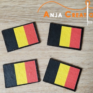 Puede incluir: Cuatro parches de tela con el diseño de la bandera belga en negro, amarillo y rojo. Los parches están sobre una superficie de madera.