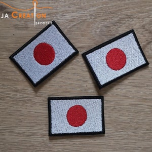 May include: Three embroidered patches of the Japanese flag. The flag is white with a large red circle in the centre. The patches are different sizes and have black borders.