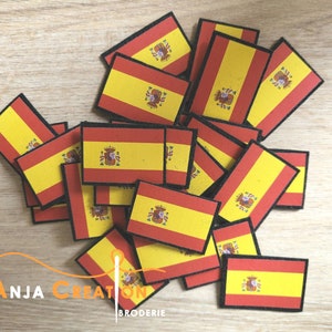 Op de afbeelding: Een stapel kleine, rechthoekige stoffen patches met de Spaanse vlag. De vlag is rood en geel met een wapenschild in het midden. De patches zijn perfect om een ​​Spaanse touch toe te voegen aan knutselwerk en projecten.