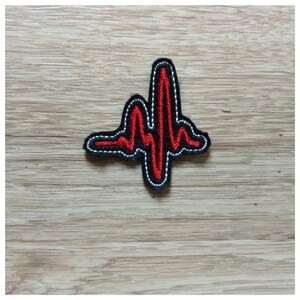 以下が含まれることがあります： 黒いアウトラインと白いステッチが付いた赤い刺繍の心臓の鼓動のパッチ