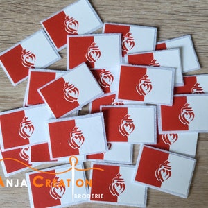 May include: A pile of white and red felt patches with a stylised heart design. The patches are rectangular and have a white background with a red heart design on the left side. The text "Anja Creation Broderie" is visible at the bottom of the image.