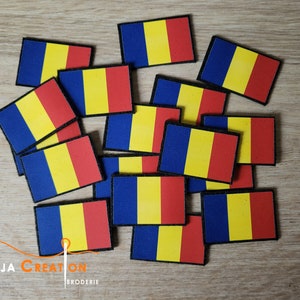 May include: A pile of small, rectangular patches featuring the Romanian flag. The flag is blue, yellow, and red. The patches are made of fabric and have a black border.