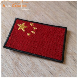 Op de afbeelding: Een rood geborduurd patch met een gele vijfpuntige ster en vier kleinere gele sterren in de linkerbovenhoek. De patch heeft een zwarte rand.