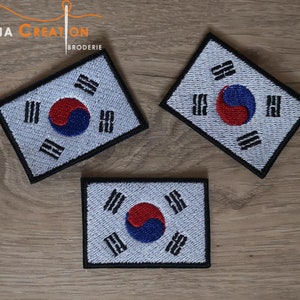Puede incluir: Tres parches bordados de la bandera de Corea del Sur sobre una superficie de madera. Los parches son blancos con un borde negro y presentan el diseño de la bandera de Corea del Sur con un símbolo yin-yang rojo y azul en el centro.