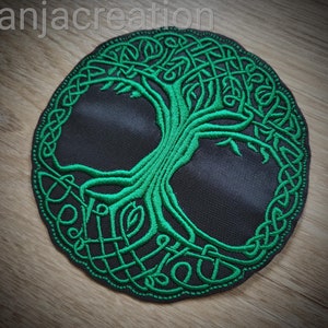 Può includere: Toppa ricamata verde con un albero della vita celtico su sfondo nero. L'albero è circondato da un disegno circolare di nodi.