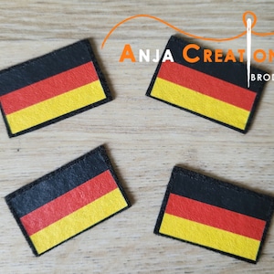 Könnte beinhalten: Vier schwarze Filzpatches mit den Farben der deutschen Flagge: Schwarz, Rot und Gelb. Die Patches liegen auf einer Holzoberfläche. Der Text "Anja Creation Broderie" ist im Hintergrund sichtbar.