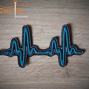 Peut inclure: Patch brodé en forme de battement de cœur bleu et noir. Le patch est sur une surface en bois.