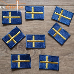 May include: Nine embroidered iron-on patches featuring the Swedish flag. The flag is blue with a yellow cross.