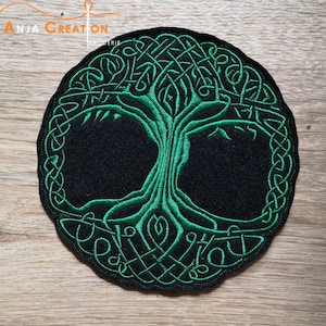 Op de afbeelding: Groen geborduurd Keltisch levensboom patch op een zwarte achtergrond. De patch is rond en heeft een gedetailleerd ontwerp met ingewikkelde knopen en spiralen.