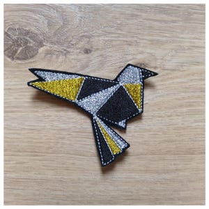 May include: A black, silver, and gold origami bird patch. The bird is made of fabric and has a geometric design.