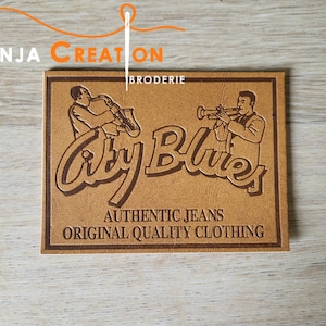 May include: Brown leather patch with the text "City Blues" in a stylised font. The patch also features two figures playing musical instruments, one with a trumpet and the other with a saxophone. The text "Authentic Jeans Original Quality Clothing" is also included on the patch.