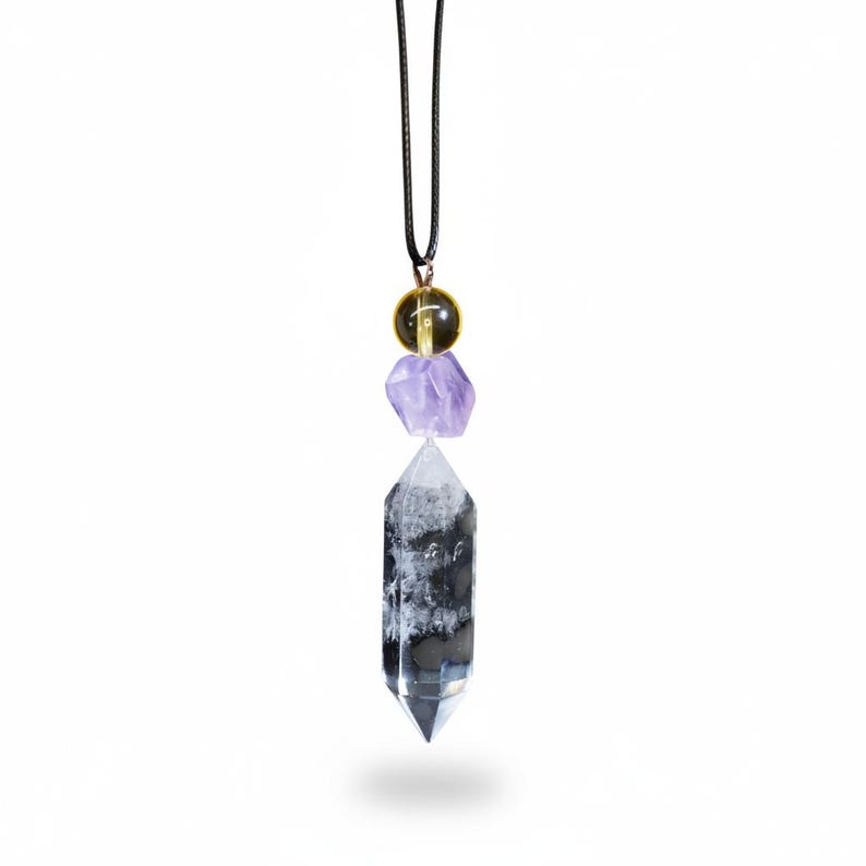 May include: A crystal pendant necklace featuring a clear quartz crystal point, a purple amethyst stone, and a yellow-green sphere. The pendant hangs from a black cord, creating a unique and eye-catching accessory.