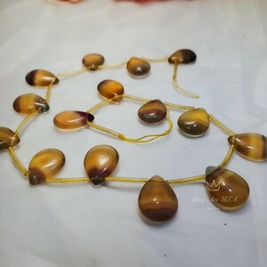 以下が含まれることがあります： 黄色、茶色、紫色の涙型の宝石ビーズのネックレス。ビーズは細い金の紐に通されています。