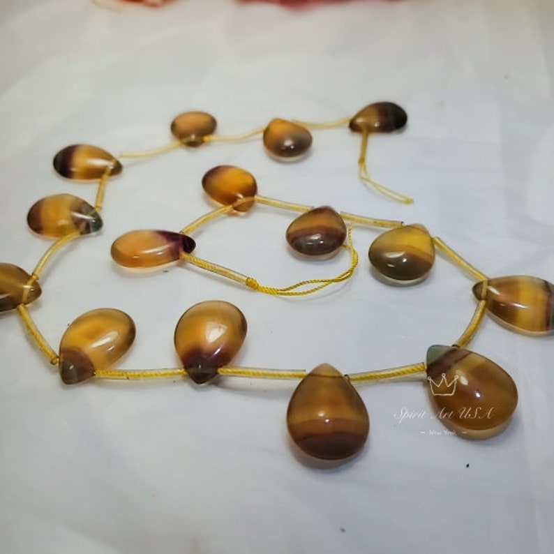 以下が含まれることがあります： 黄色、茶色、紫色の涙型の宝石ビーズのネックレス。ビーズは細い金の紐に通されています。