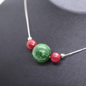 May include: A silver chain necklace with three round beads. The center bead is green and the two outer beads are red.
