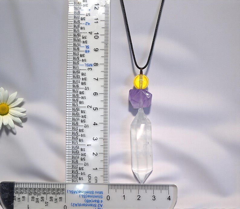 May include: A pendant necklace featuring a clear quartz crystal point, amethyst, and yellow bead accents. The necklace hangs from a black cord. The quartz crystal measures approximately 1.5 inches in length. The necklace is displayed against a white background.