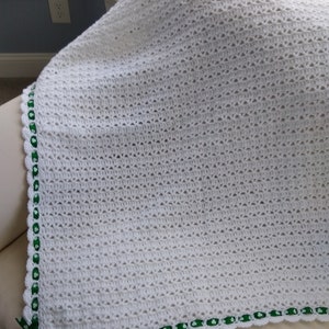 May include: White crochet baby blanket with a green shamrock ribbon trim.