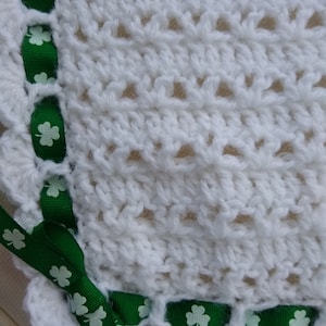 May include: White crocheted baby blanket with a green shamrock ribbon trim.