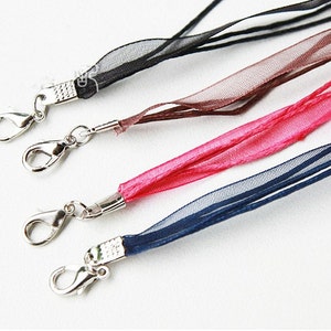 May include: Four different colored ribbon lanyards with silver lobster clasps. The ribbons are black, brown, pink, and blue.