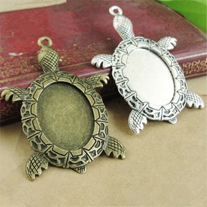 May include: Two silver and bronze turtle shaped pendant blanks with oval shaped glass cabochon settings. The turtle pendants are detailed with raised lines and textures.