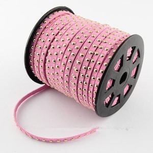 May include: A spool of pink leather trim with gold studs. The trim is rolled up on a black plastic spool.